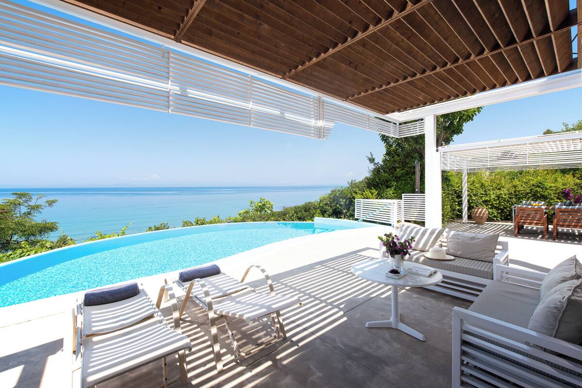 A poolside area with lounge chairs, a table with a vase of flowers, and a view of the sea.