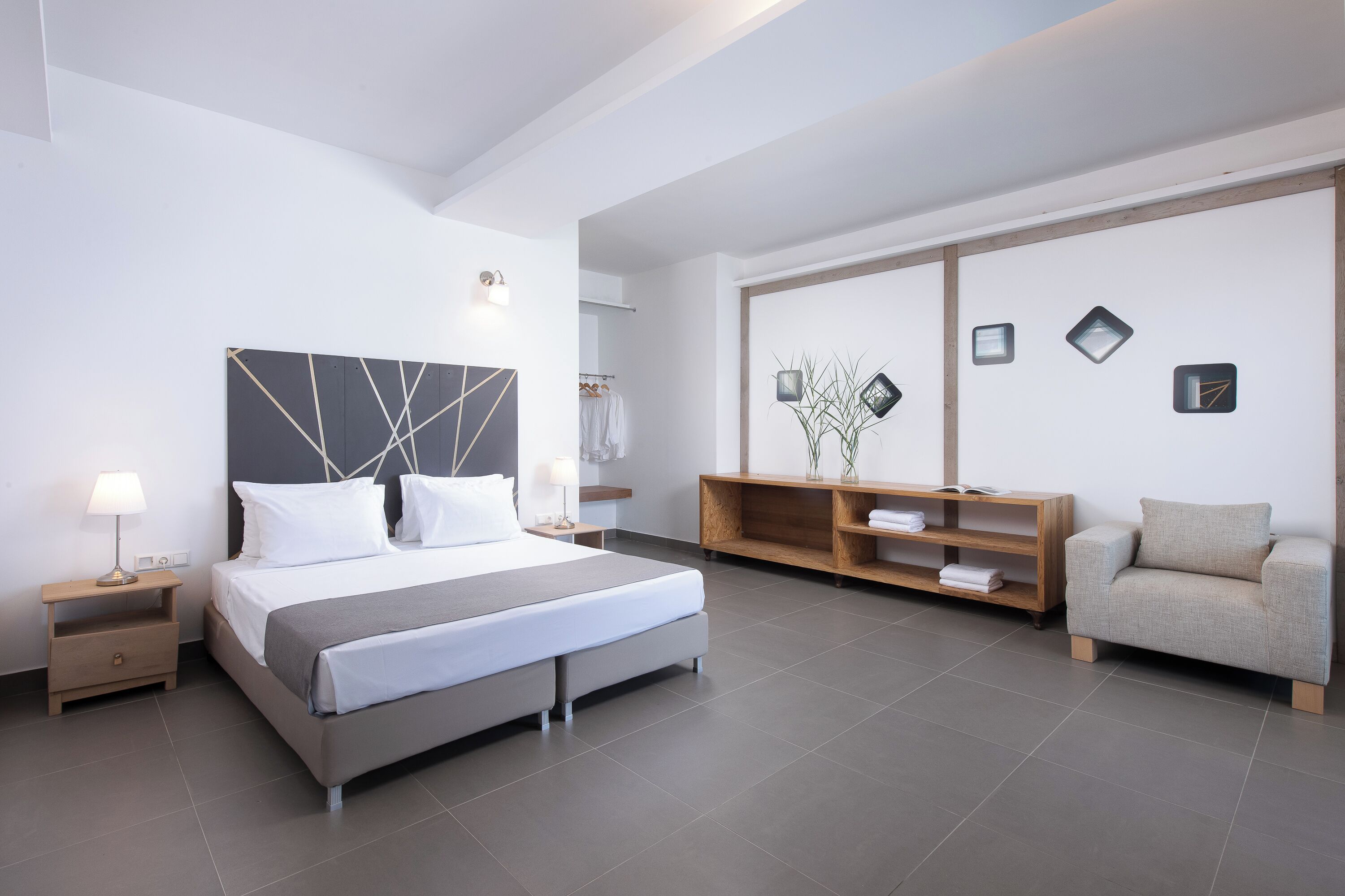 A modern hotel room with a large bed, bedside tables, a wooden console, a sofa, and a large mirror.