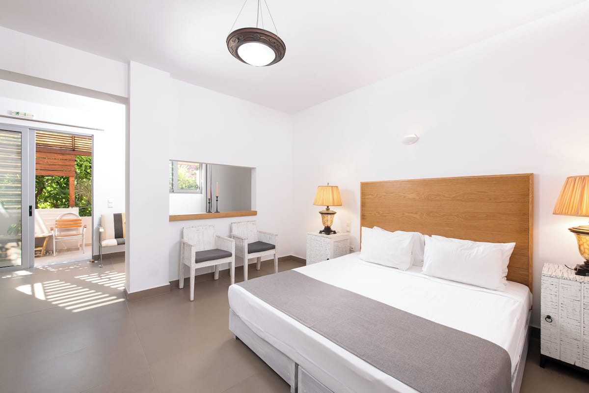 A hotel room with a bed, two bedside tables, a chair, a desk, a mirror, and a view of the outdoors.