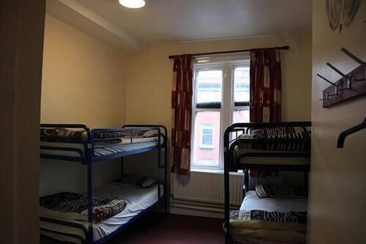 A dormitory room with two bunk beds, a window with curtains, and a radiator.