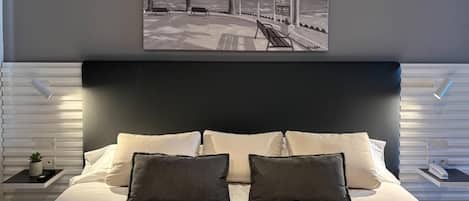 Ein modernes Schlafzimmer mit einem großen Bett, einem dunklen Kopfteil und einem Kunstwerk mit Strandmotiv darüber.