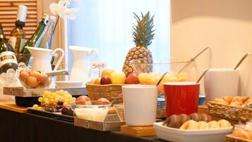 Een buffettafel met diverse etenswaren en dranken, waaronder fruit, een ananas en een flesje met de tekst 'RIGOL'.