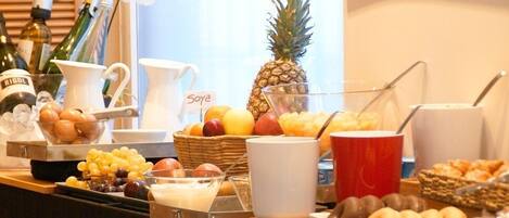 Una mesa de buffet con diversos alimentos y bebidas, incluyendo frutas, una piña y una botella con la etiqueta "RIGOL".