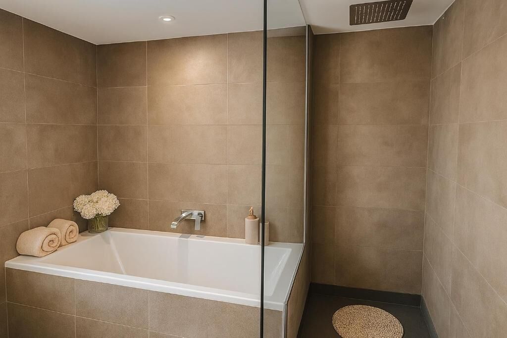 A modern bathroom with a large bathtub, a glass shower enclosure, and a small round rug on the floor.
