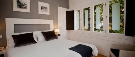 Une chambre avec un grand lit, une tête de lit, deux tables de chevet, une commode, une lampe et une fenêtre donnant sur un paysage verdoyant.