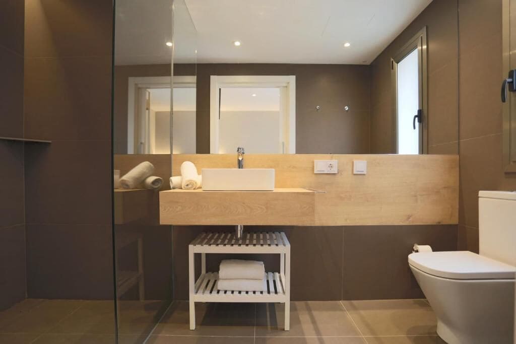 A modern bathroom with a glass shower enclosure, a wooden vanity, and a white toilet.