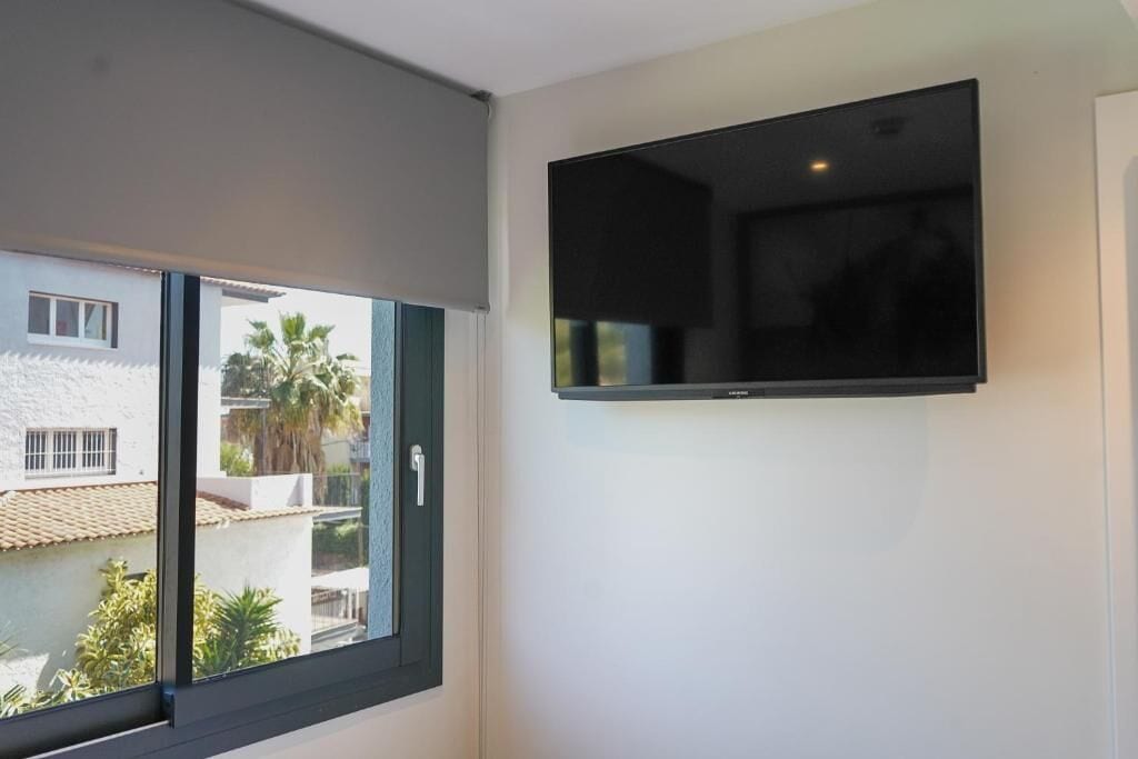 A room with a large window, a flat-screen TV mounted on the wall, and a view of neighboring buildings.