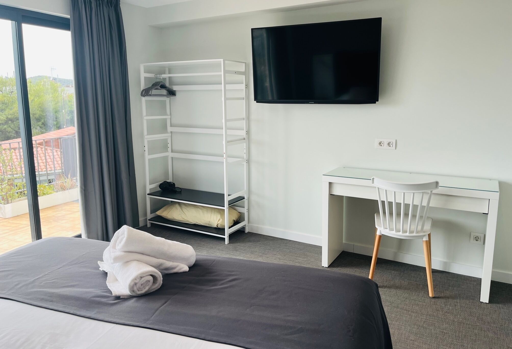 Une chambre d’hôtel comprenant un lit, un bureau, une télévision, une armoire et un balcon.