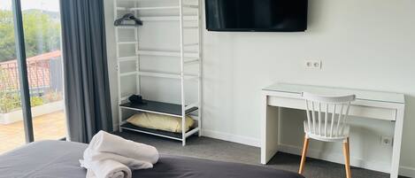 Une chambre d’hôtel comprenant un lit, un bureau, une télévision, une armoire et un balcon.