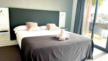 Habitación de hotel con una cama grande, un cabecero oscuro y vistas a un balcón con palmeras.