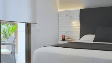 Habitación de hotel moderna con una cama grande, una mesita de noche con una vela roja y vistas al balcón.