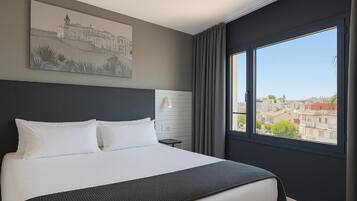 Quarto de hotel moderno com uma cama grande, vista da cidade através de uma janela ampla e um quadro na parede.