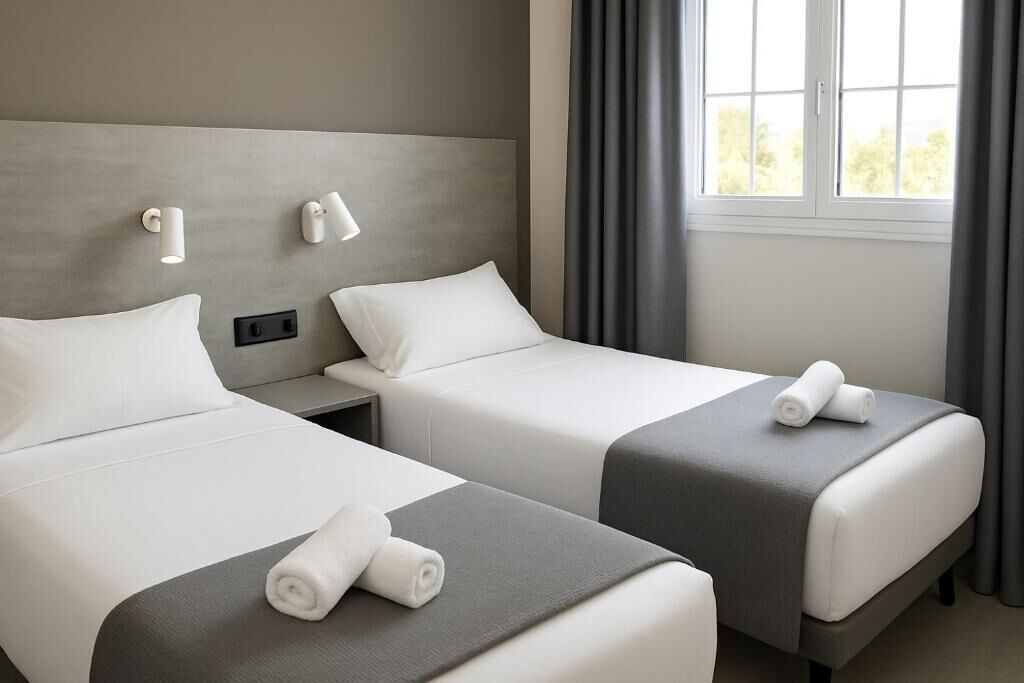 Une chambre d’hôtel avec deux lits, une fenêtre avec des rideaux et des lampes fixées au mur.