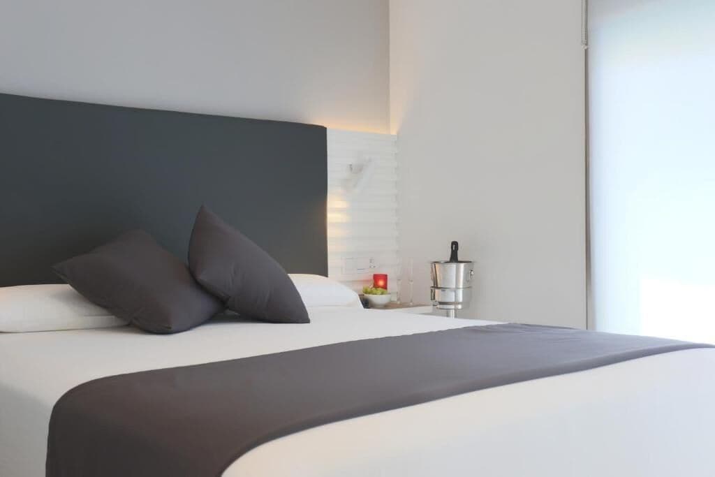 A modern hotel room with a large bed, dark headboard, and a bedside table with a red candle.