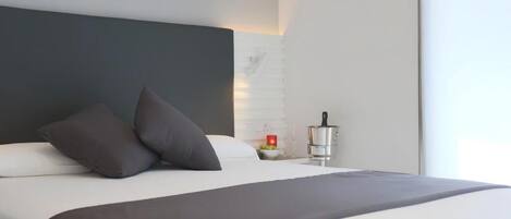 A modern hotel room with a large bed, dark headboard, and a bedside table with a red candle.