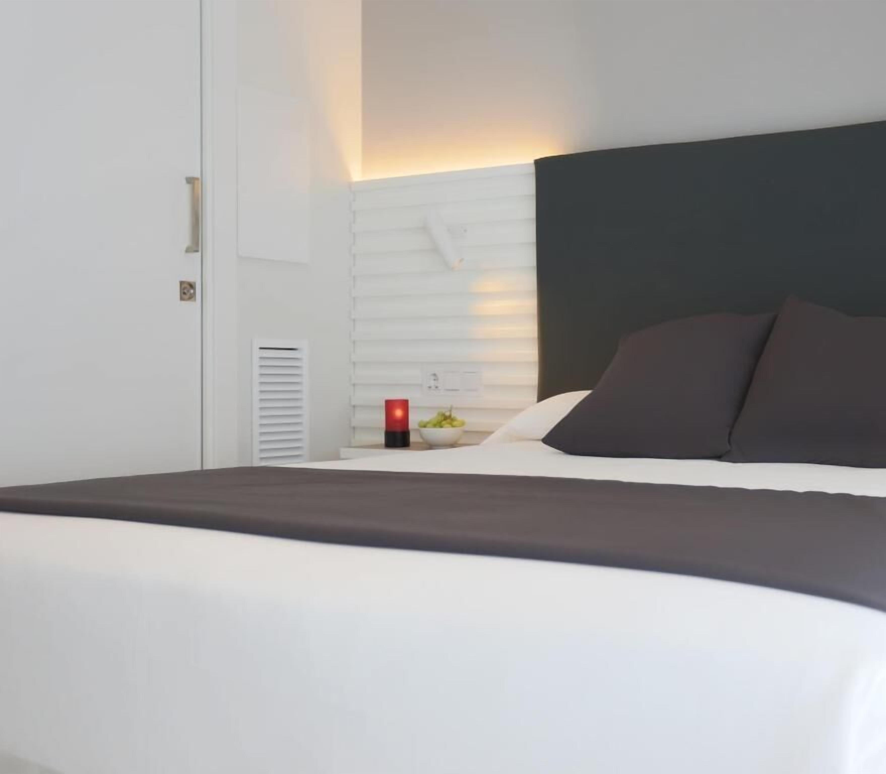 A modern hotel room with a large bed, a bedside table with a red lamp, and a wall-mounted heater.