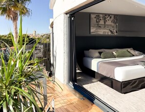 A modern bedroom with a bed, pillows, and a view of the cityscape. - Hotel Sitges (Sitges)