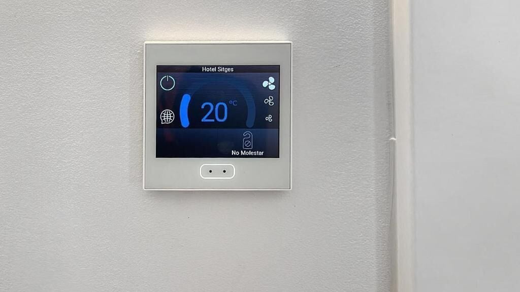 A digital thermostat on a wall displaying the temperature as 20°C, with a power button and a "No Molestar" (Do Not Disturb) indicator.