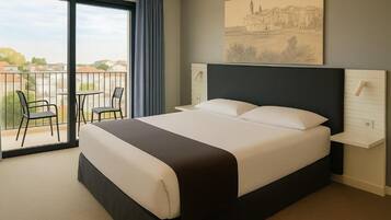 Habitación de hotel con una cama grande, balcón con sillas y vistas a la ciudad.