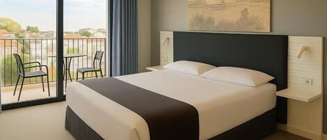 Habitación de hotel con una cama grande, balcón con sillas y vistas a la ciudad.
