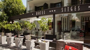 A hotel exterior with outdoor seating, potted plants, and a red bicycle. - Hotel Sitges (Sitges)