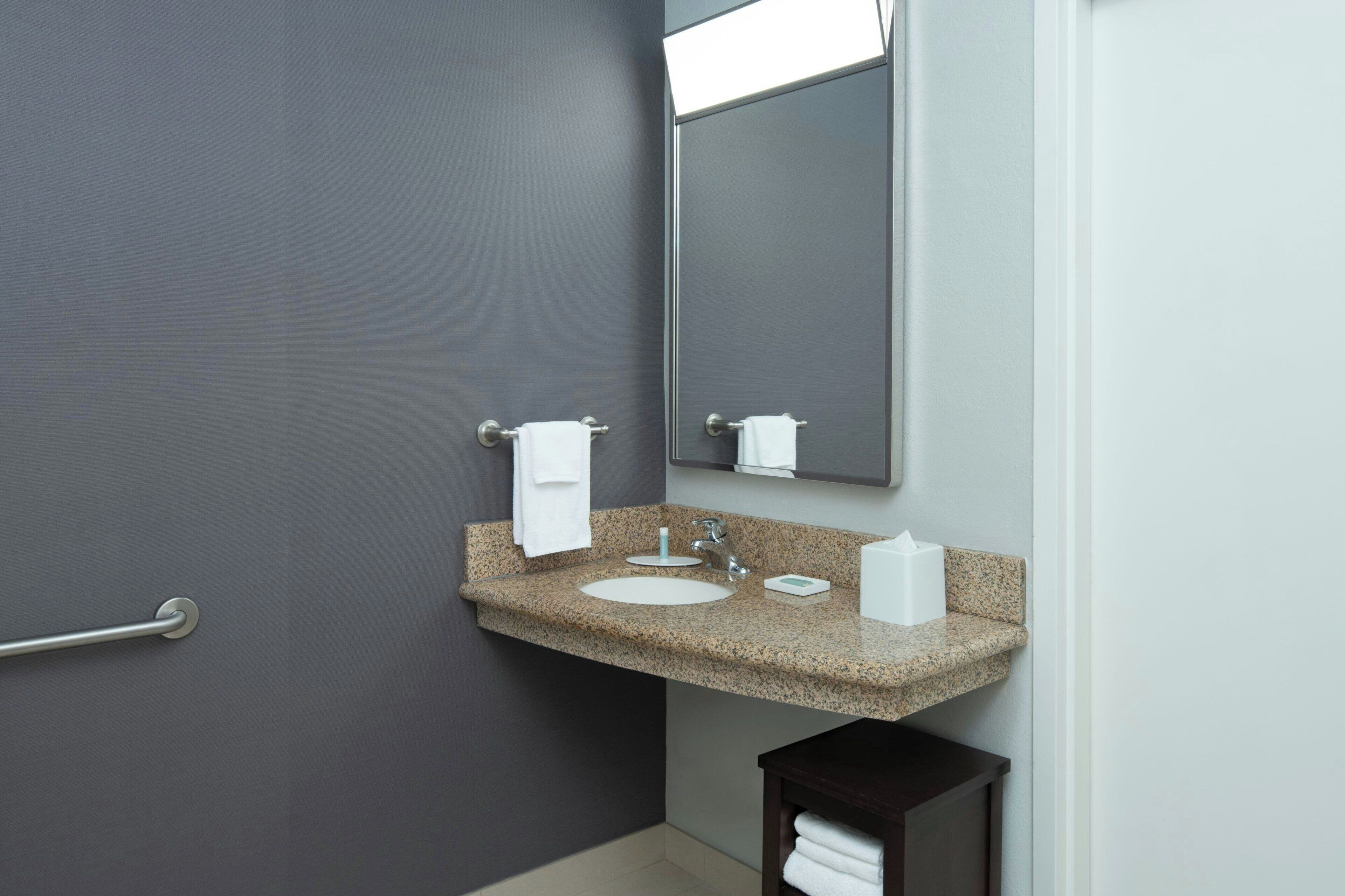 A bathroom with a granite countertop sink, a mirror, a towel rack, and a small dark wooden cabinet.