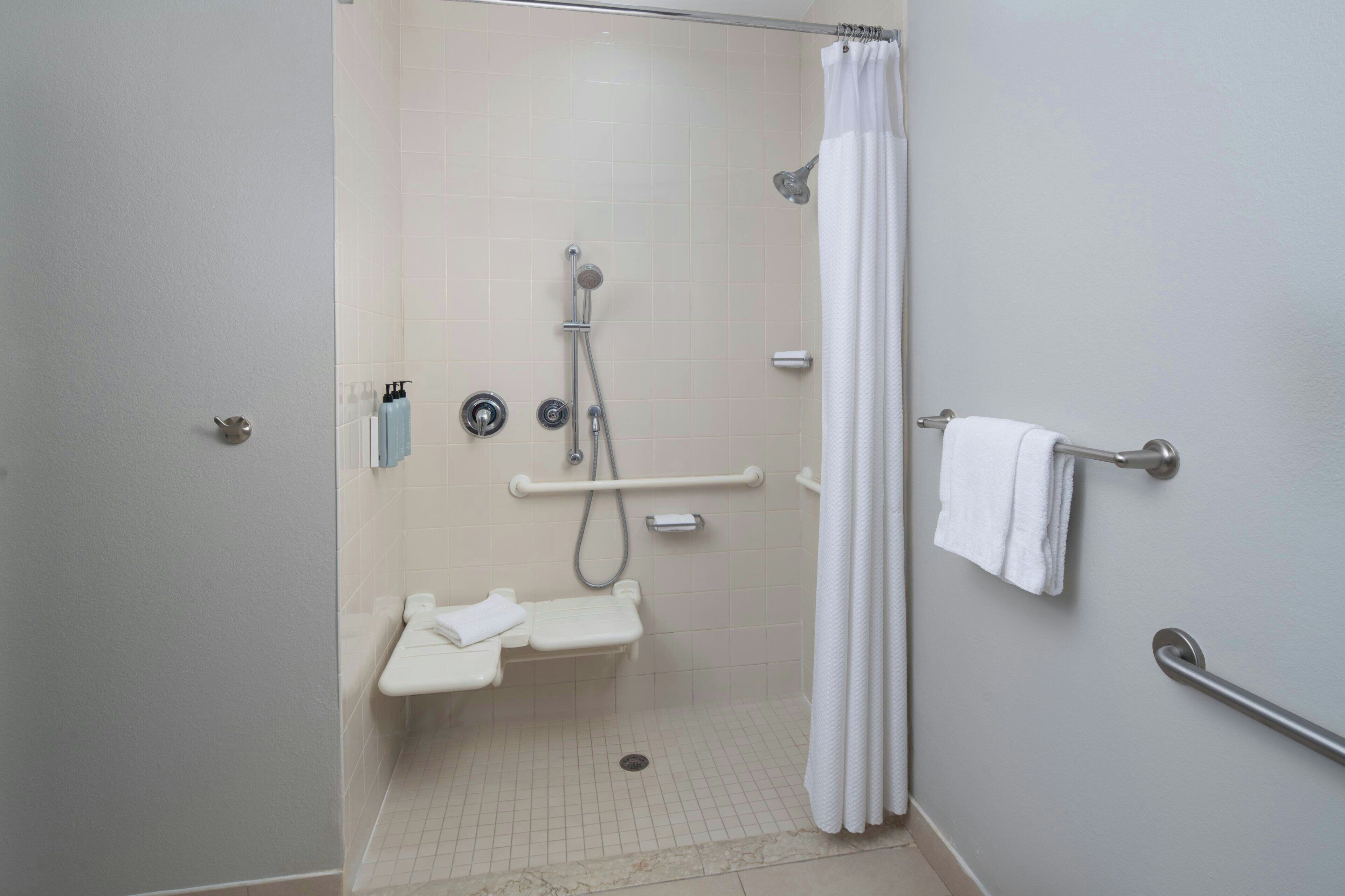 Un baño con ducha, barras de apoyo, toallero y retrete.
