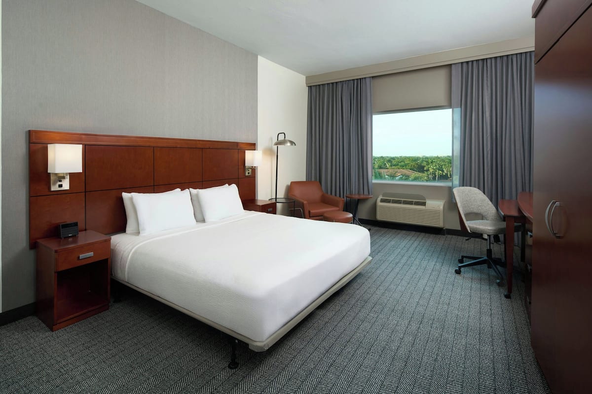 A hotel room with a large bed, a desk, a chair, and a window with curtains.