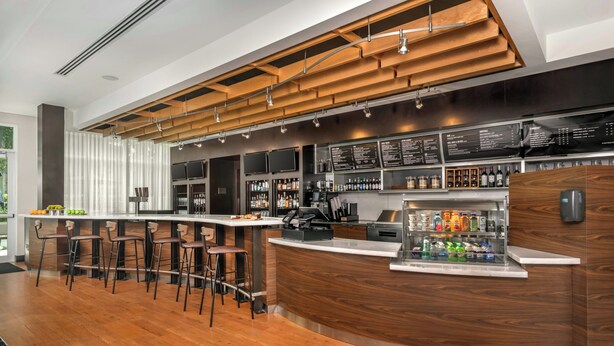 A modern bar area with wooden accents, bar stools, a beverage dispenser, and a menu board.