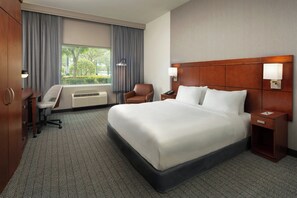 Habitación de hotel con una cama grande, un escritorio con silla, una mesita y una ventana con cortinas.