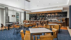 A modern restaurant with multiple dining tables and chairs, a bar area with shelves of bottles, and a large window with curtains.
