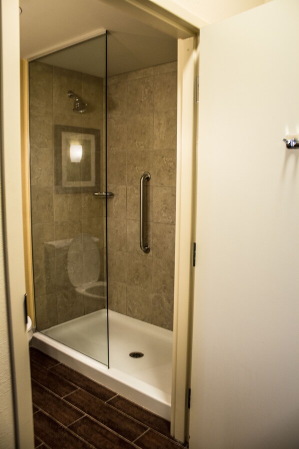 A glass-enclosed shower area with a white door, a visible toilet, and a tiled floor.
