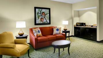 Habitación de hotel con sofá, sillón, mesa de centro y una zona de kitchenette.