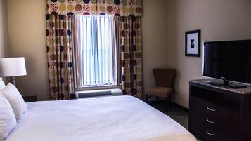 A hotel room with a large bed, a television, a chair, and a desk with drawers.