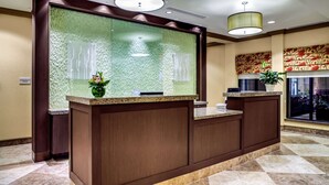 A reception desk with a green textured backdrop, a potted plant, and a check-in counter. - Hilton Garden Inn Pittsburgh/Cranberry (Cranberry Township)