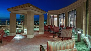 An outdoor patio area with seating and a covered section, featuring large windows and a view of the street. - Hilton Garden Inn Pittsburgh/Cranberry (Cranberry Township)