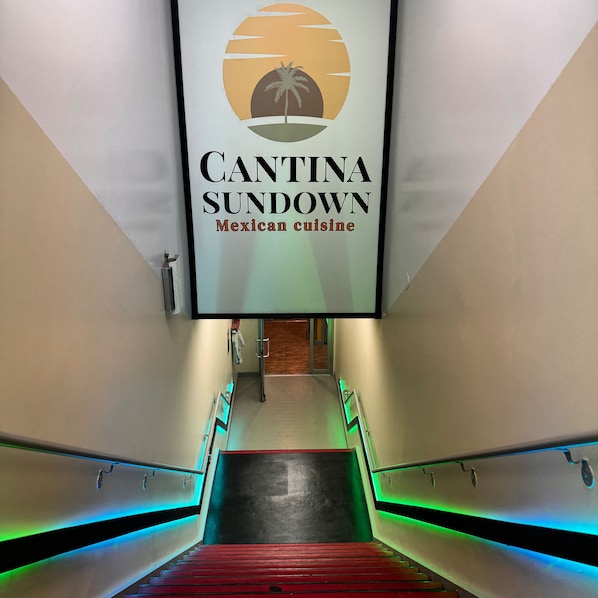 Un pasillo con un letrero que indica Cantina Sundown, cocina mexicana, que conduce a una habitación con piso de madera y una puerta.