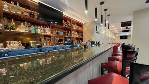 A bar area with a long counter, multiple shelves of liquor bottles, and red bar stools. - Holiday Inn NYC - Lower East Side by IHG (New York)