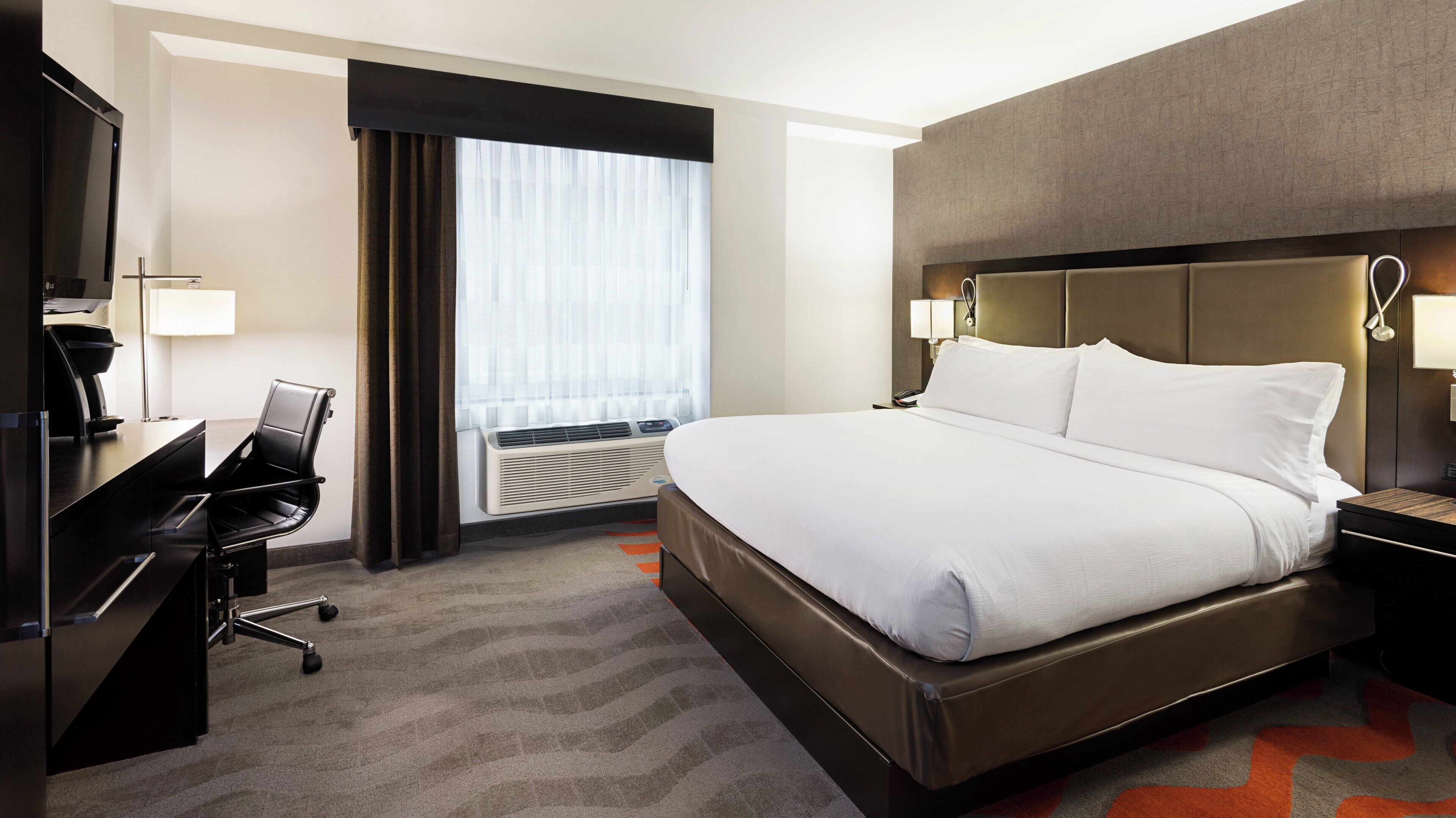 A hotel room with a bed, desk, chair, and a window with curtains.