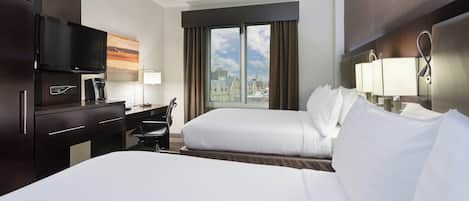 Habitación de hotel con cama, escritorio, silla, televisor y ventana con vista a la ciudad.
