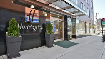 A hotel entrance with a glass facade, a sign reading 'Holiday Inn', and a green mat at the door.