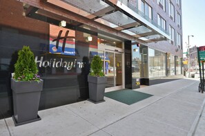 A hotel entrance with a glass facade, a sign reading 'Holiday Inn', and a green mat at the door. - Holiday Inn NYC - Lower East Side by IHG (New York)