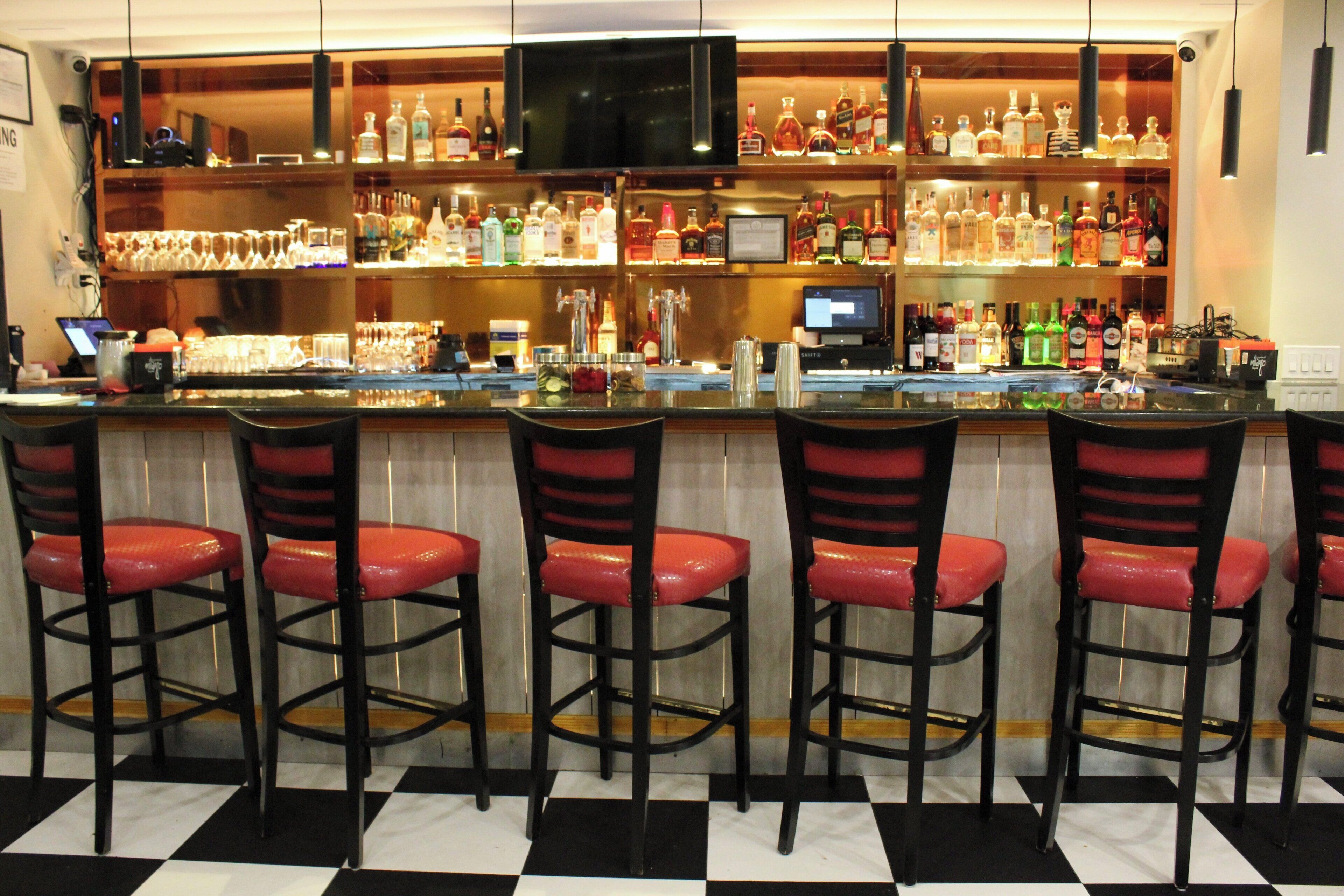 Un bar con varios taburetes y una gran variedad de botellas de licor.
