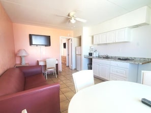 A compact living space with a kitchenette, a dining area, and a seating area with a couch and chairs. - The Caprice Motel (Wildwood)