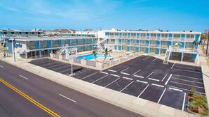 A hotel with a pool, multiple floors, and a parking lot. - The Caprice Motel (Wildwood)