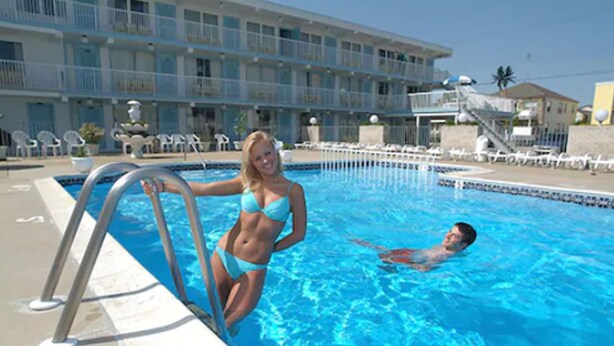 A swimming pool with a metal ladder, a person in a bikini, and a man swimming. - The Caprice Motel (Wildwood)