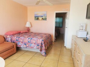 A bedroom with a bed, a sofa, a desk with a coffee maker, and a painting on the wall. - The Caprice Motel (Wildwood)