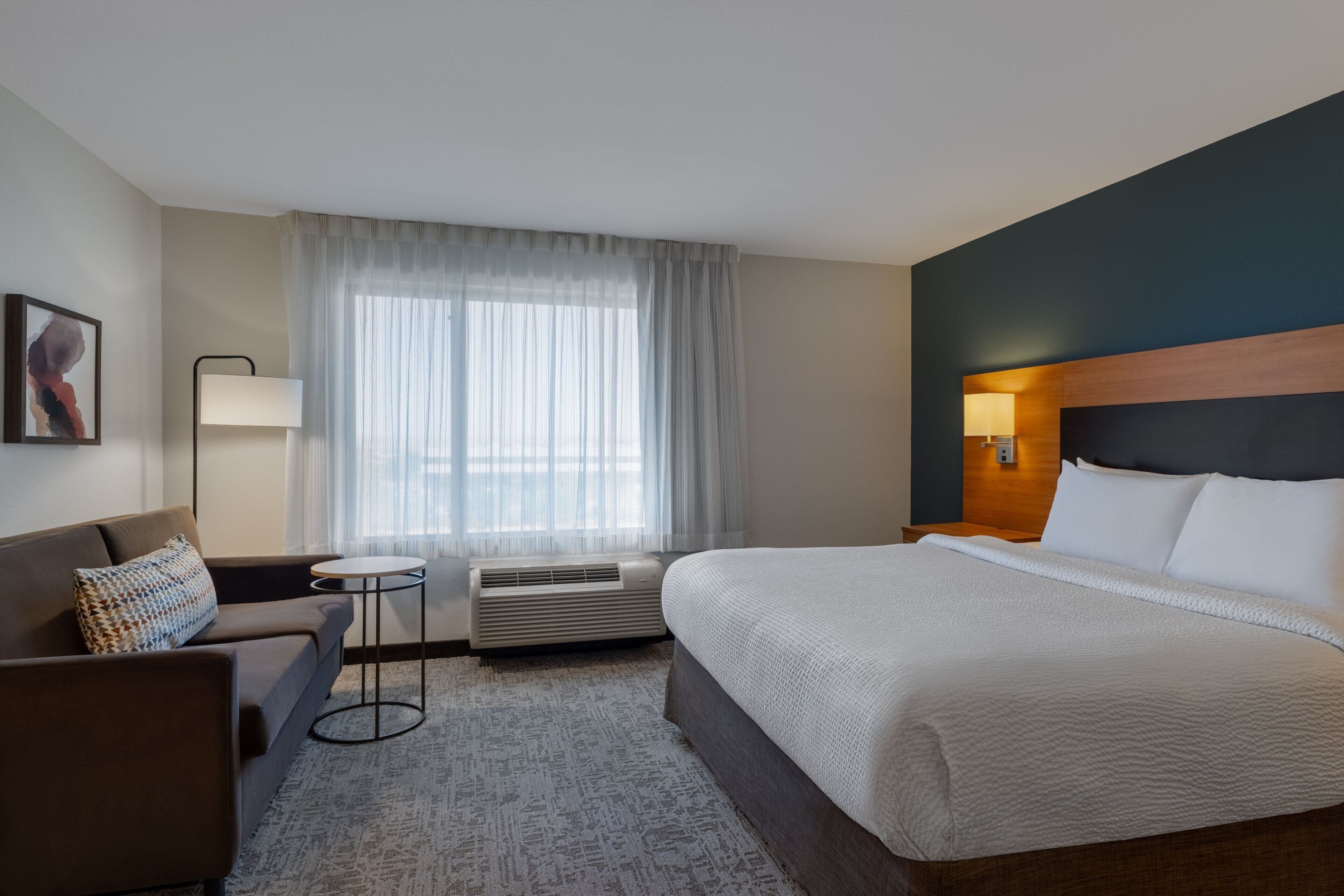 Una habitación de hotel con cama, sofá, una mesita y ventana con cortinas.