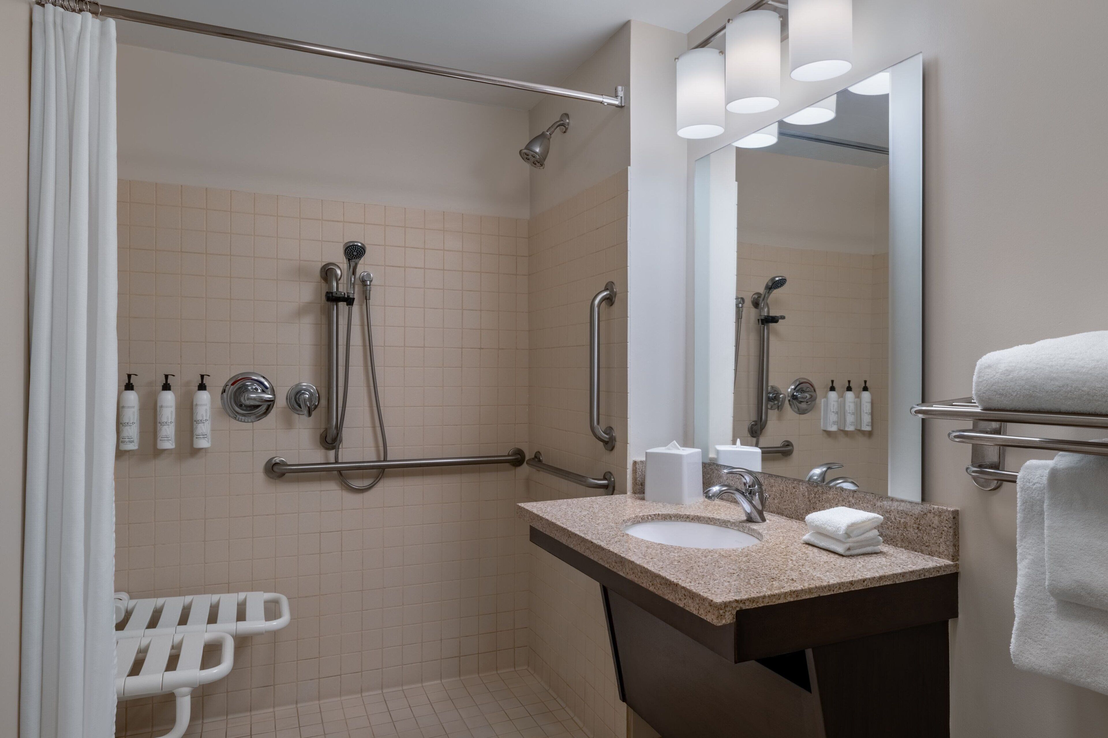 A bathroom with a shower, grab bars, a sink, and a mirror.