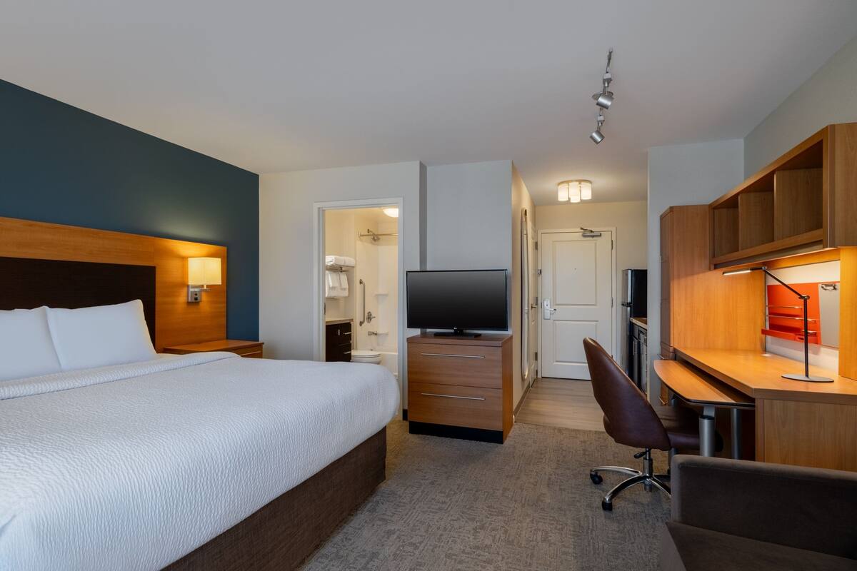 A hotel room with a large bed, a desk with a computer, a TV, and a wardrobe.